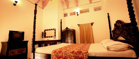 A traditional four-poster bed with a floral bedspread, a wooden dresser with a television, and a ceiling fan.
