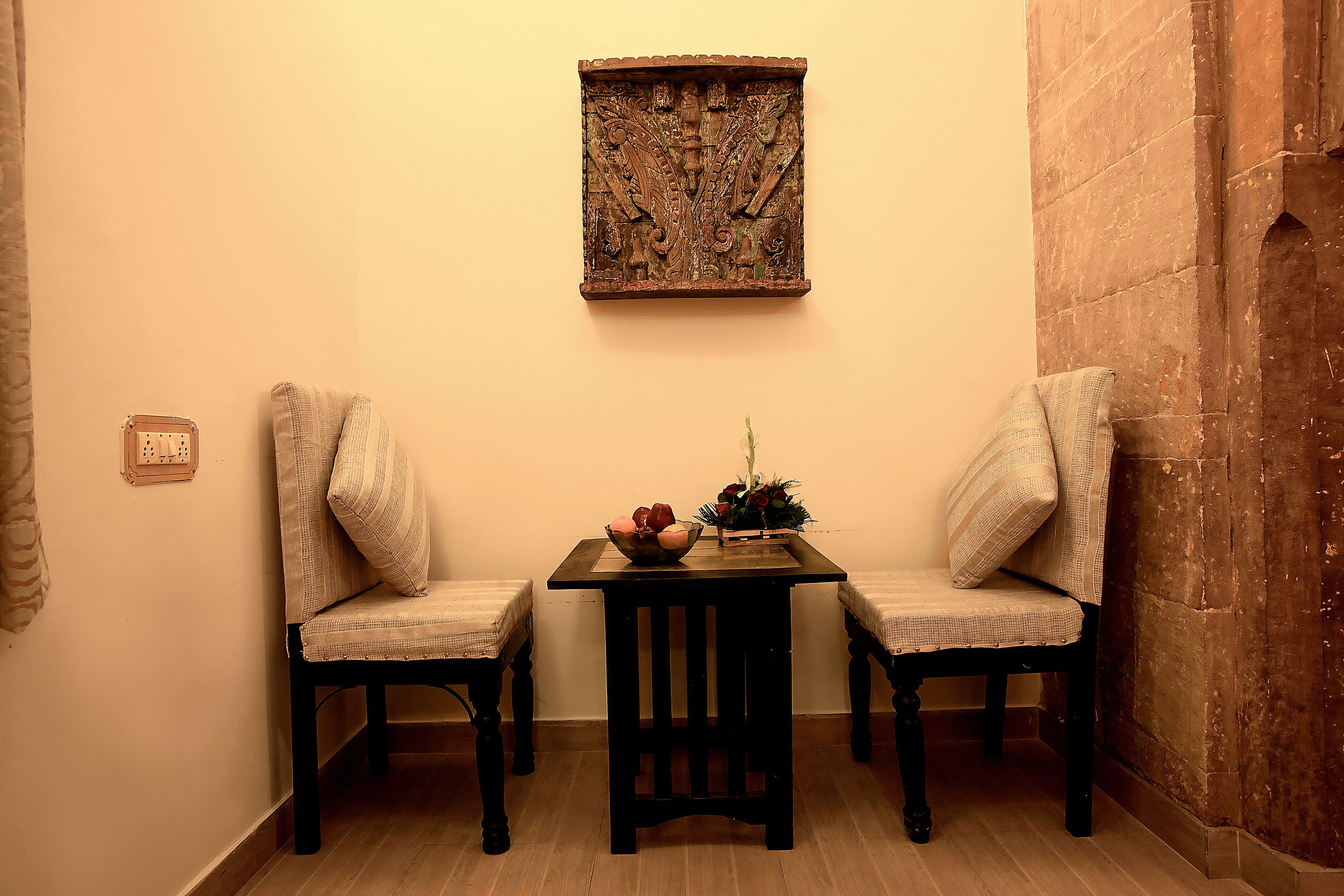 Une pièce d’angle comprenant deux fauteuils rembourrés, une petite table avec un vase et des fleurs, et un élément décoratif mural.
