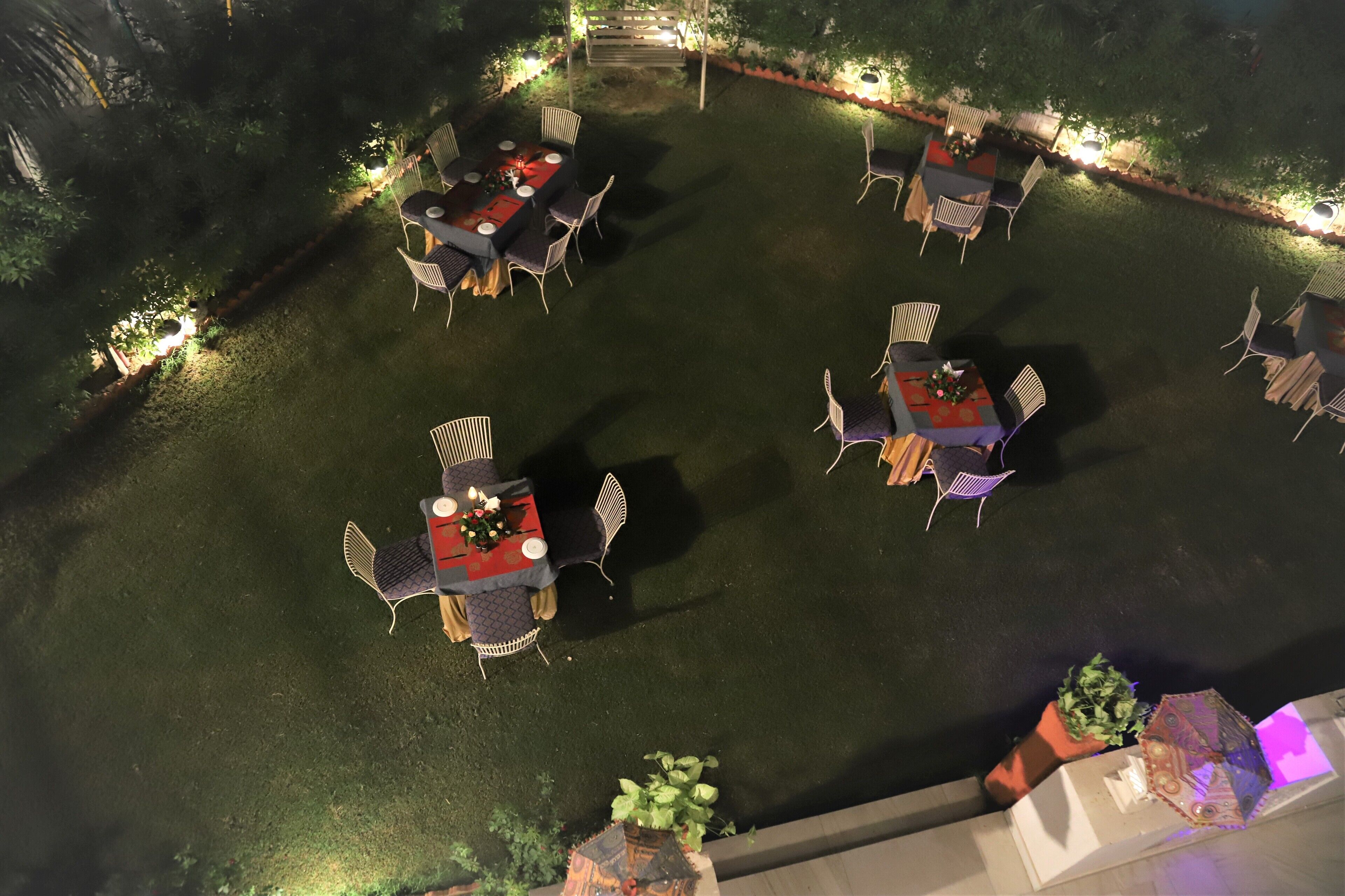 An outdoor dining area with tables and chairs arranged in a circular pattern, surrounded by a well-maintained lawn and decorative lighting.