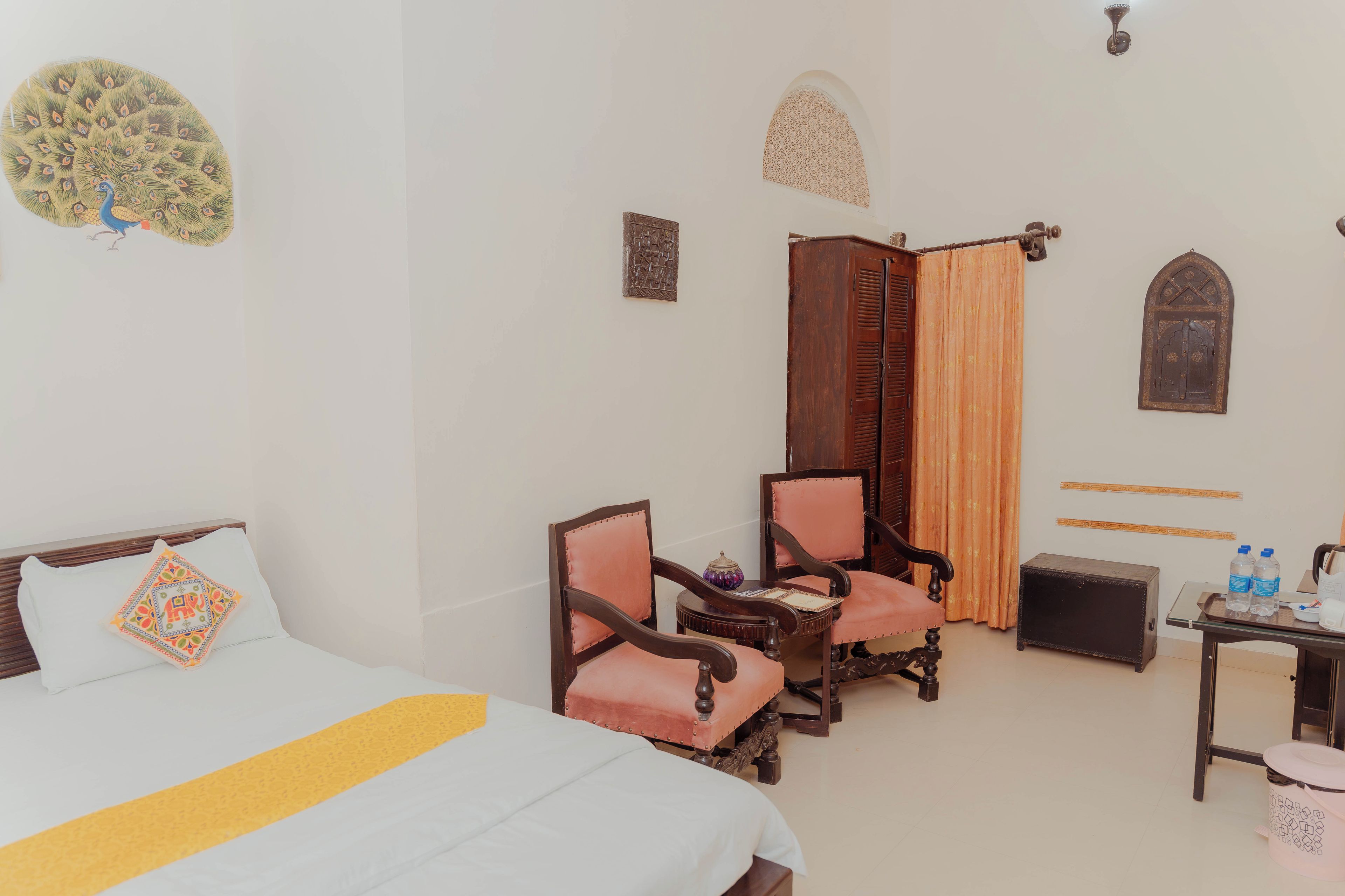 A hotel room with a bed, two chairs, a small table, a wardrobe, and a decorative wall piece.