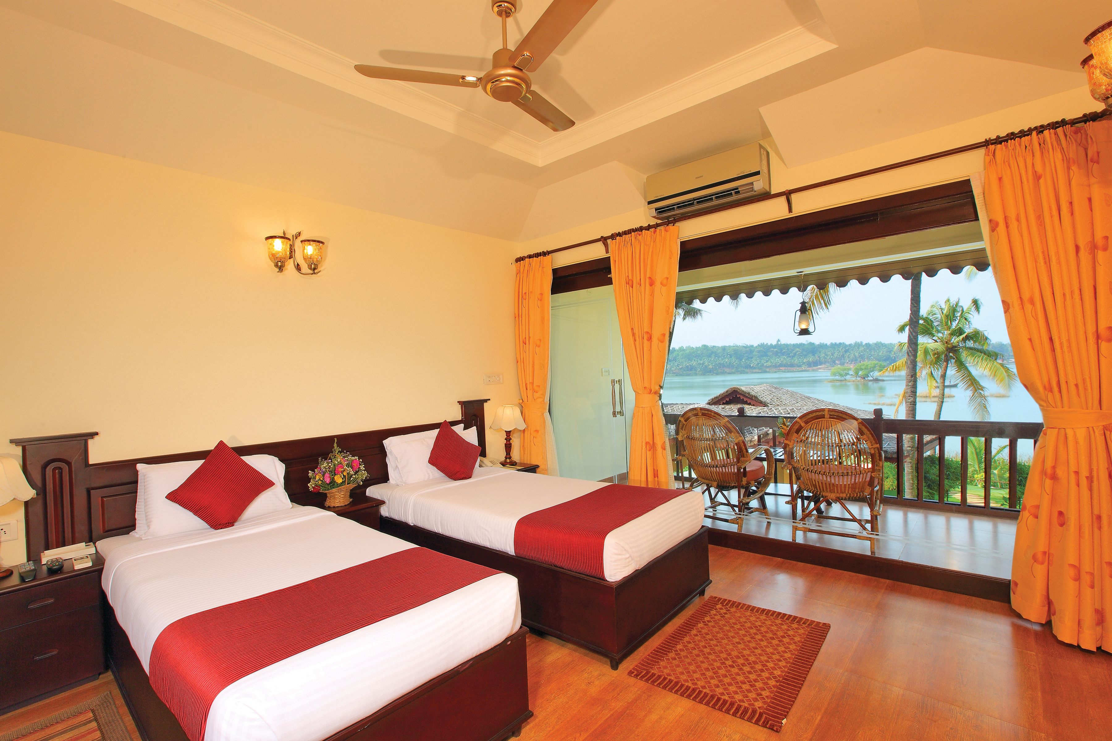 A hotel room with two beds, a ceiling fan, an air conditioning unit, a balcony with a view of the sea, and a wicker chair.