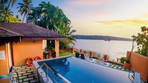 A swimming pool with steps leading up to it, surrounded by palm trees and a view of the water. - Fragrant Nature Backwater Resort & Ayurveda Spa (Kollam)
