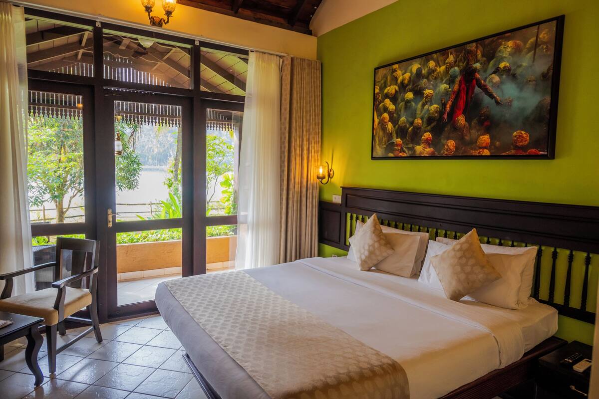 Une chambre d’hôtel avec un grand lit, un tableau au mur et une vue sur la verdure.