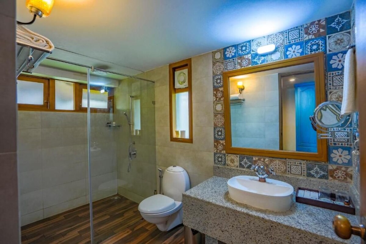 Un baño con cabina de ducha de vidrio, inodoro blanco, lavabo con encimera de granito y salpicadero de azulejos con diseño floral.