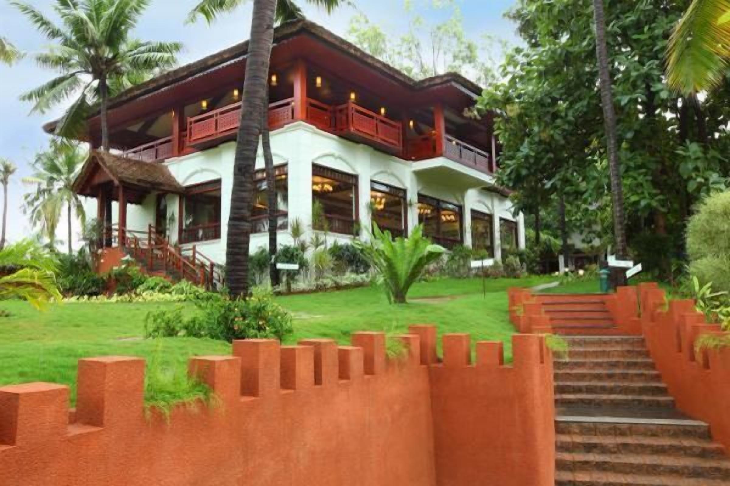 A two-story building with a balcony, surrounded by lush greenery and palm trees.