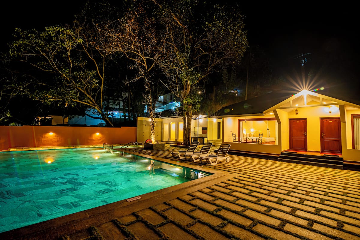 Une piscine avec des chaises longues et un bâtiment dont l’entrée est bien éclairée.