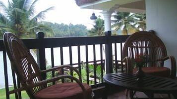 A balcony with two wicker chairs and a small table, overlooking a lush green landscape with palm trees.