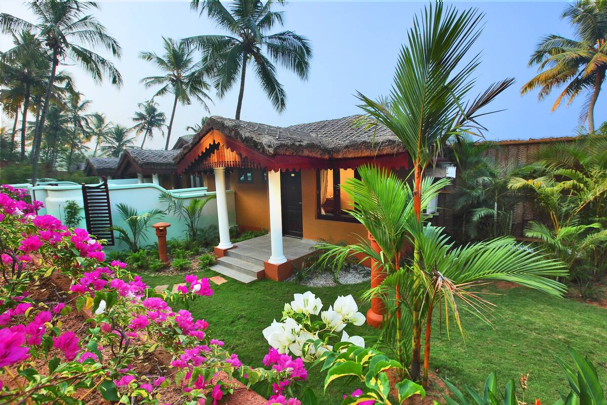 Un complexe hôtelier tropical doté de bungalows aux toits de chaume, d’une végétation luxuriante et de palmiers.