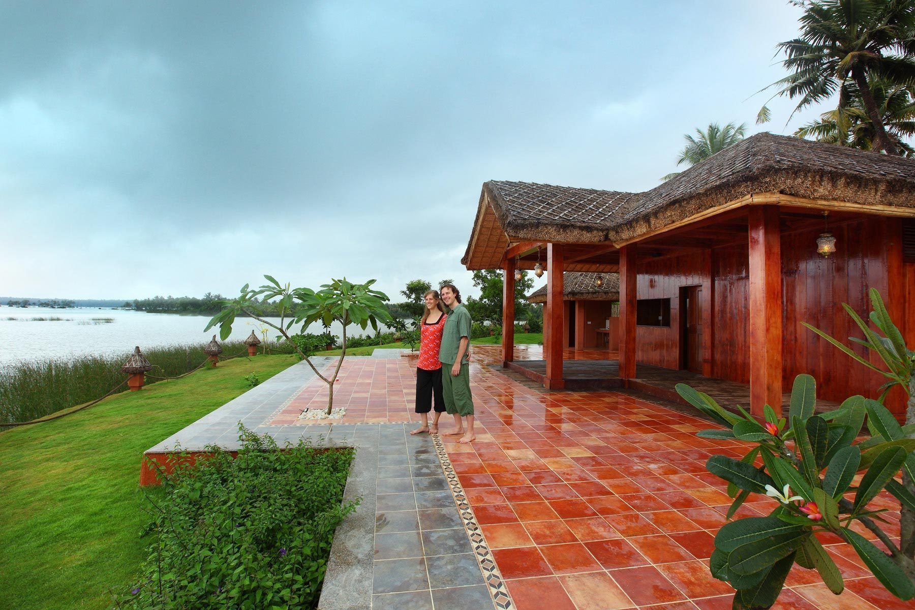 A wooden structure with a tiled floor, surrounded by greenery and a body of water.