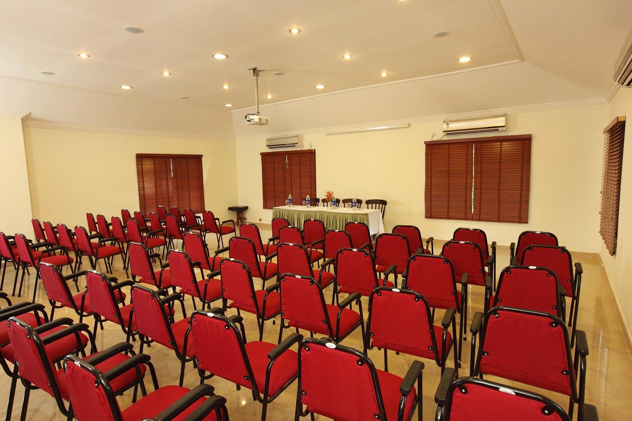 Uma sala de conferências com fileiras de cadeiras vermelhas, um projetor e unidades de ar condicionado.