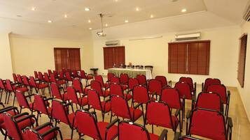 Uma sala de conferências com fileiras de cadeiras vermelhas, um projetor e unidades de ar condicionado.
