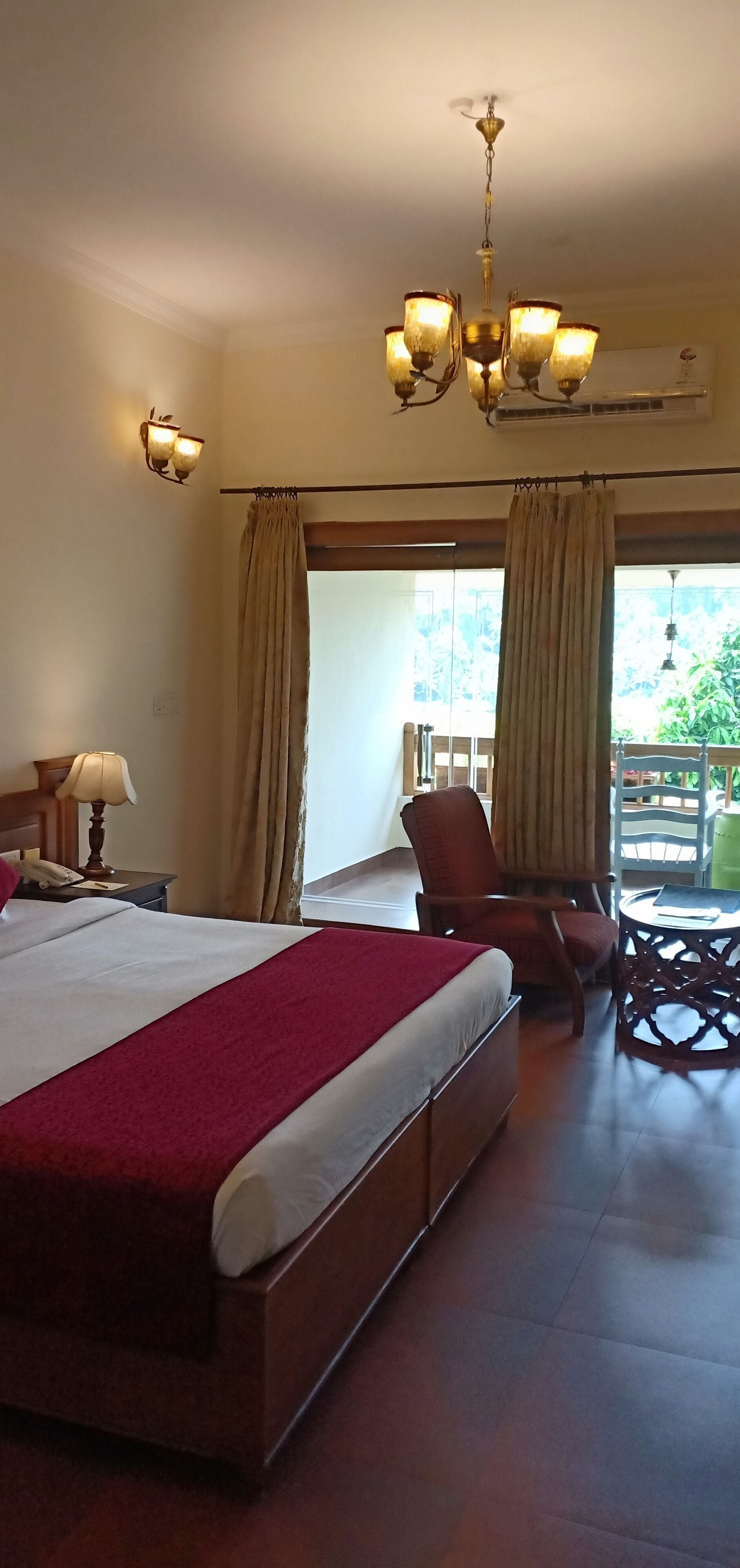 Habitación de hotel con una cama grande, una silla, una mesa, un candelabro y vistas al exterior.
