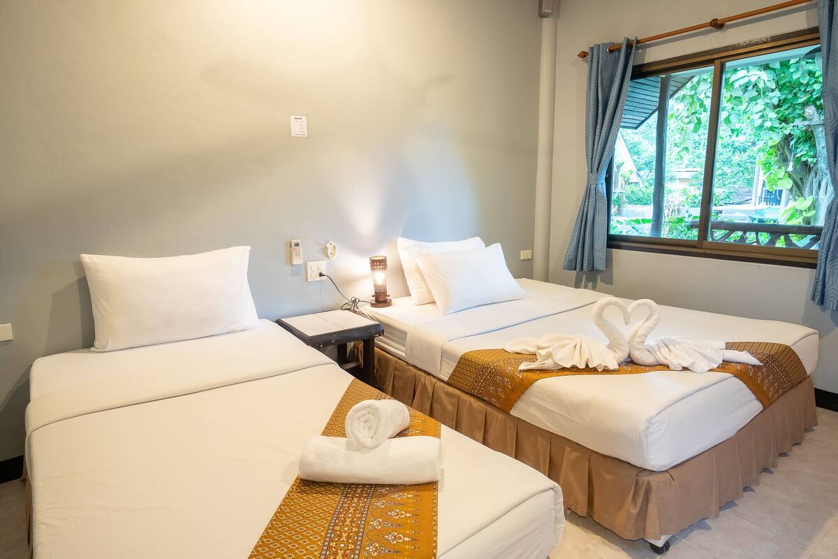 Quarto de hotel com duas camas, uma mesa de cabeceira, um abajur e uma janela com cortinas.