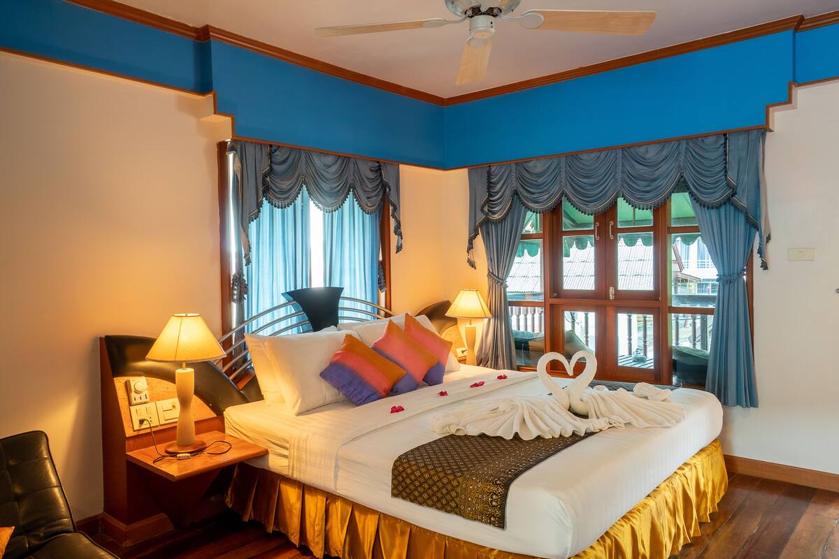 Quarto de hotel com cama, mesa de cabeceira, abajur, cadeira e janela com cortinas.