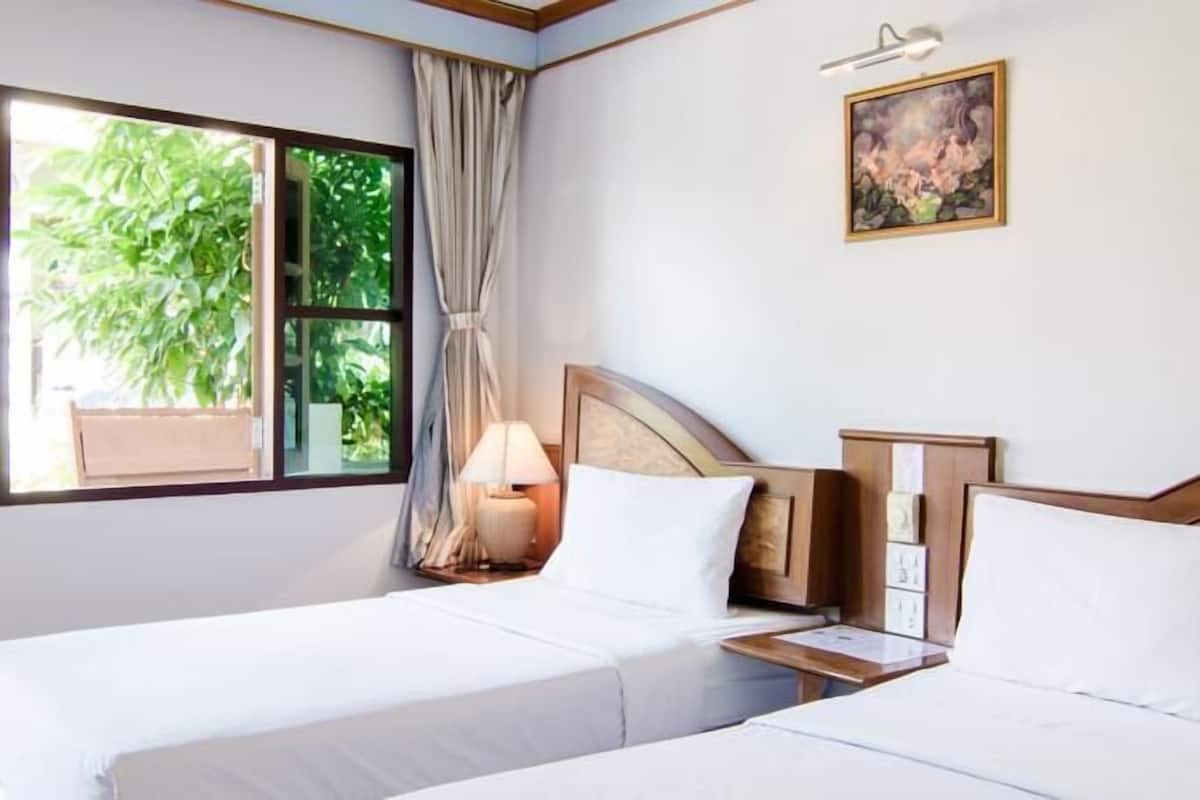 Quarto de hotel com duas camas, uma janela com cortinas, uma mesa de cabeceira com abajur e um quadro na parede.