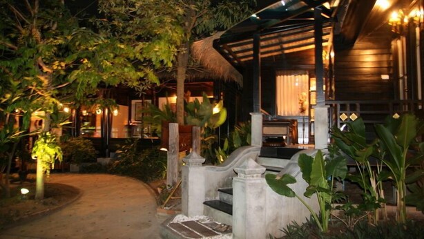 A wooden building with a thatched roof, surrounded by lush greenery and a paved pathway leading to the entrance. - Sea Garden Resort - Haad Rin (Ko Pha-ngan)