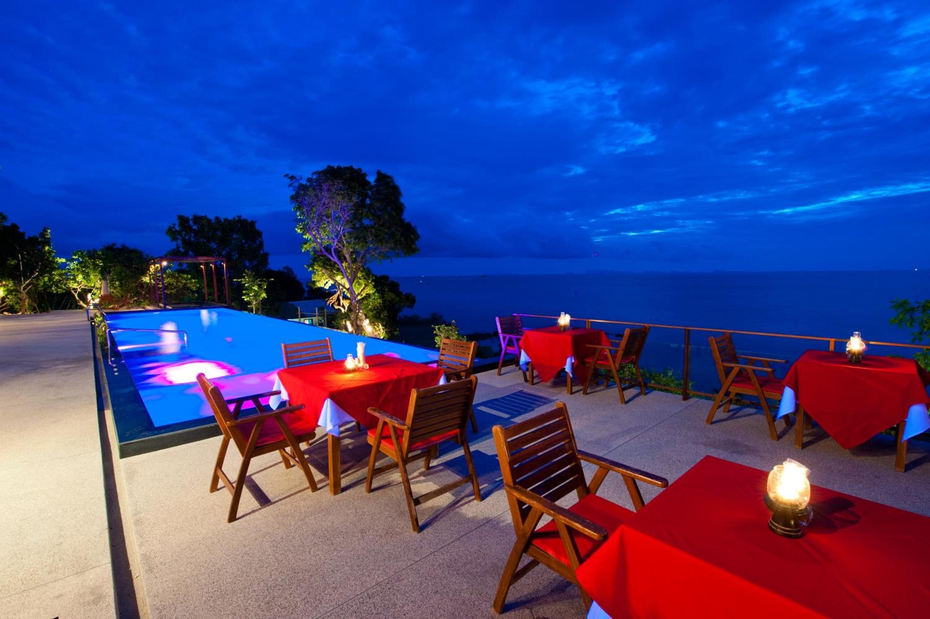 An outdoor dining area with tables and chairs, a pool, and a view of the sea.
