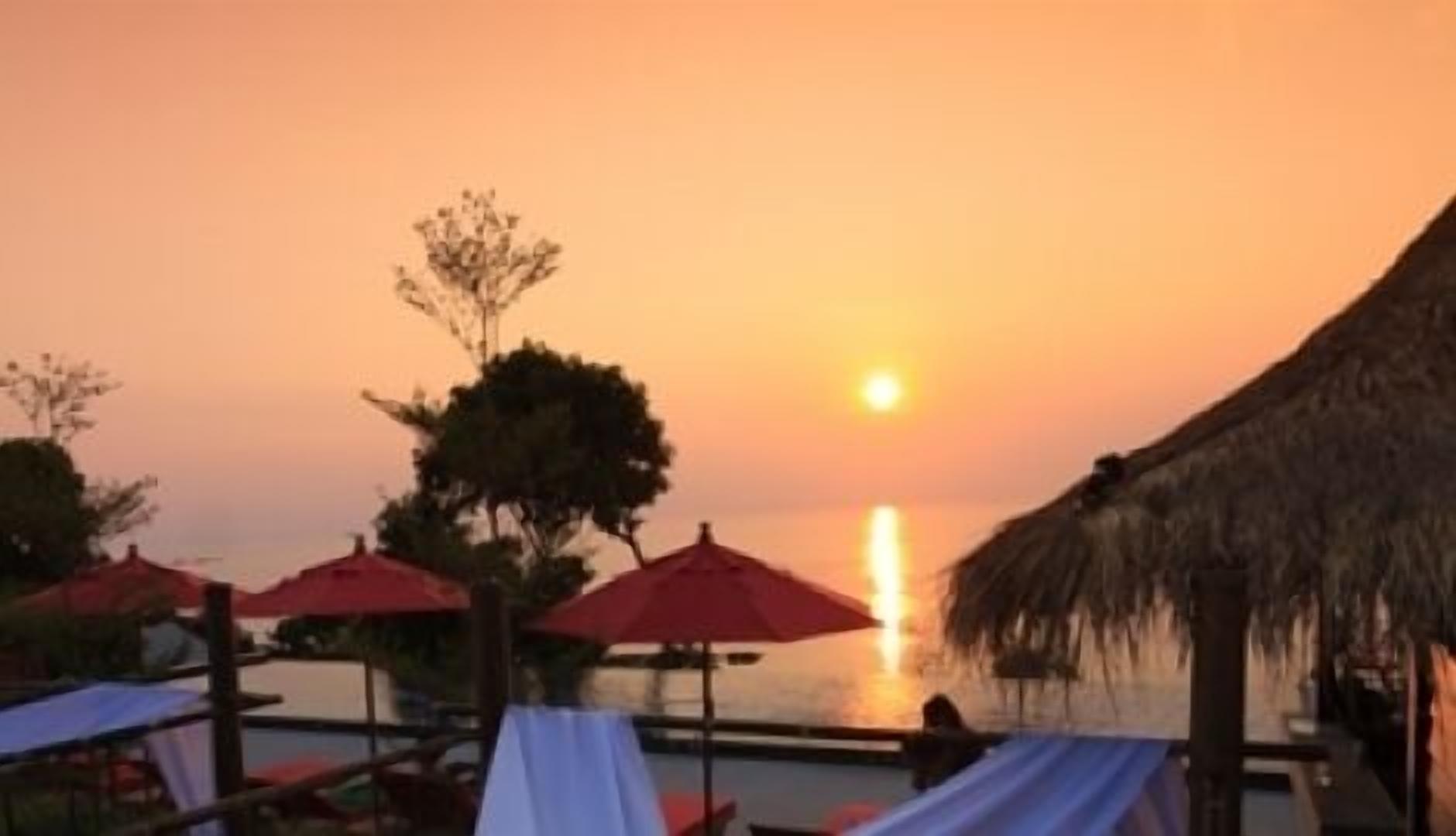 A sunset view with beach umbrellas and a thatched roof structure.