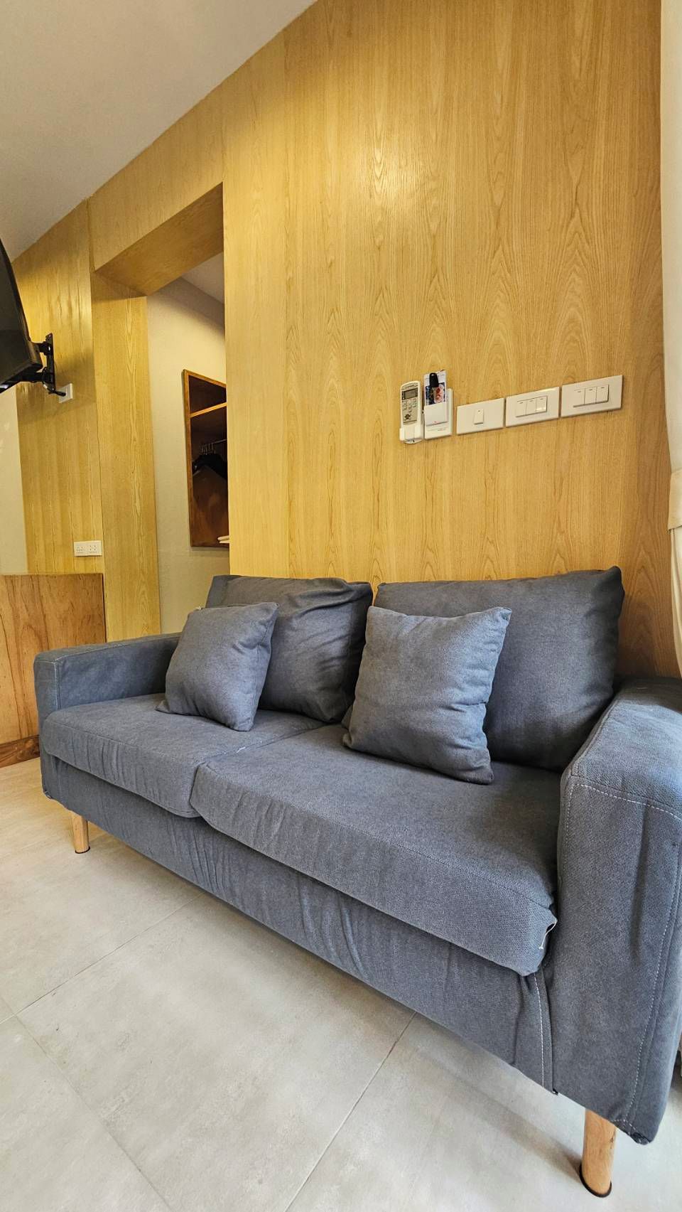 Un sofá gris con paneles de madera en la pared de fondo.
