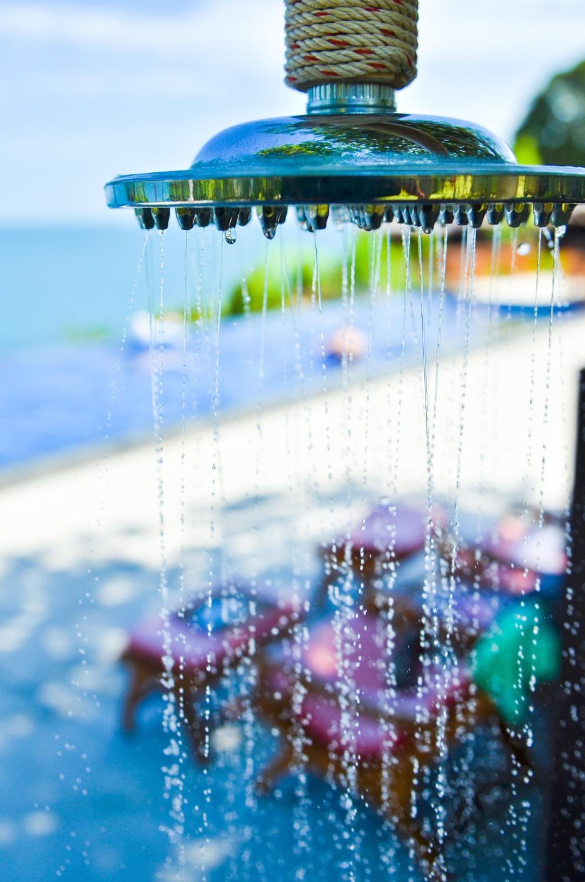 Una fuente con un tirador de cuerda, agua cayendo y un fondo borroso que muestra una piscina y sombrillas.