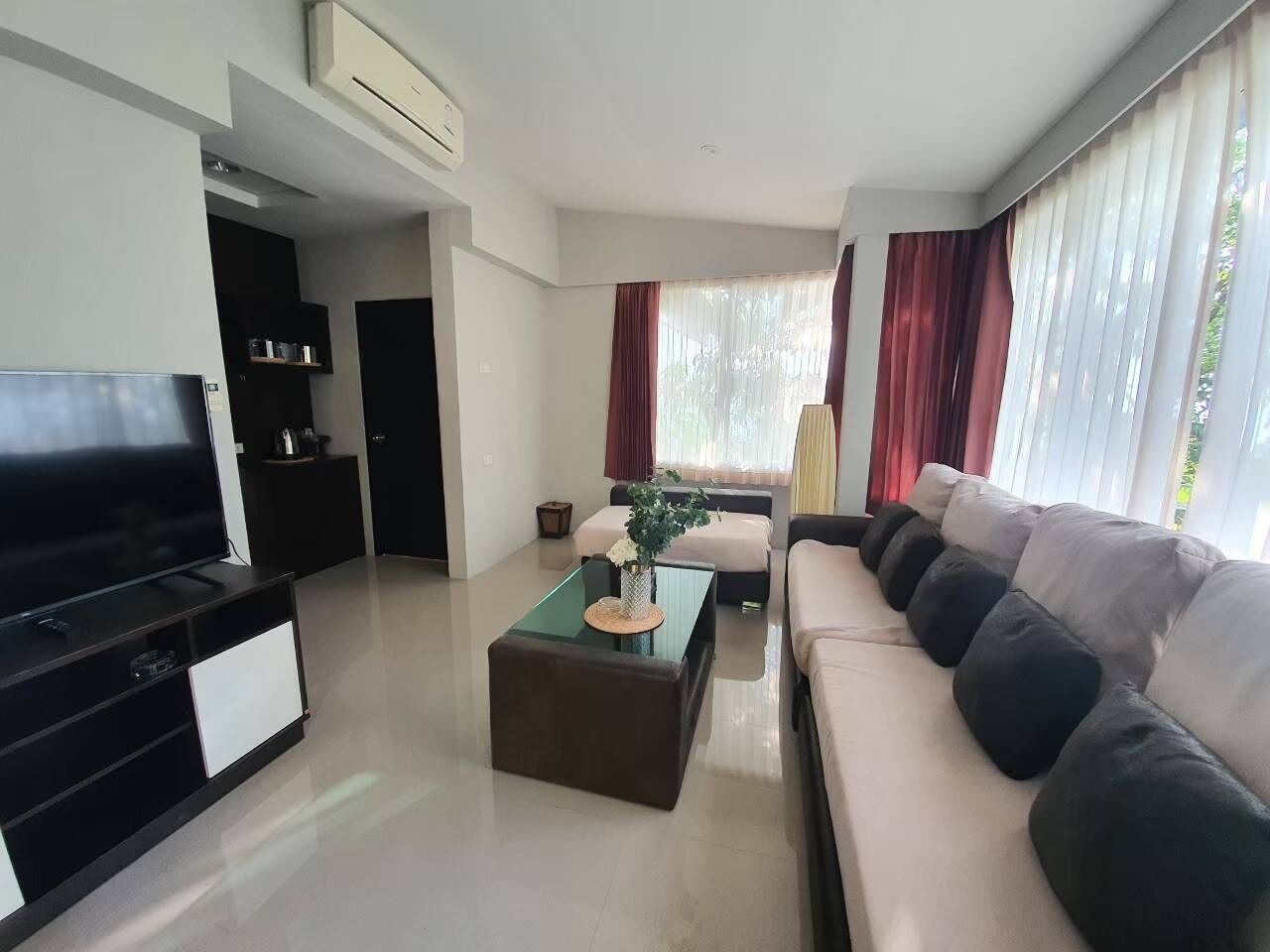 A modern living room with a flat-screen TV, a glass coffee table, a sofa, and a dining area with a black cabinet.
