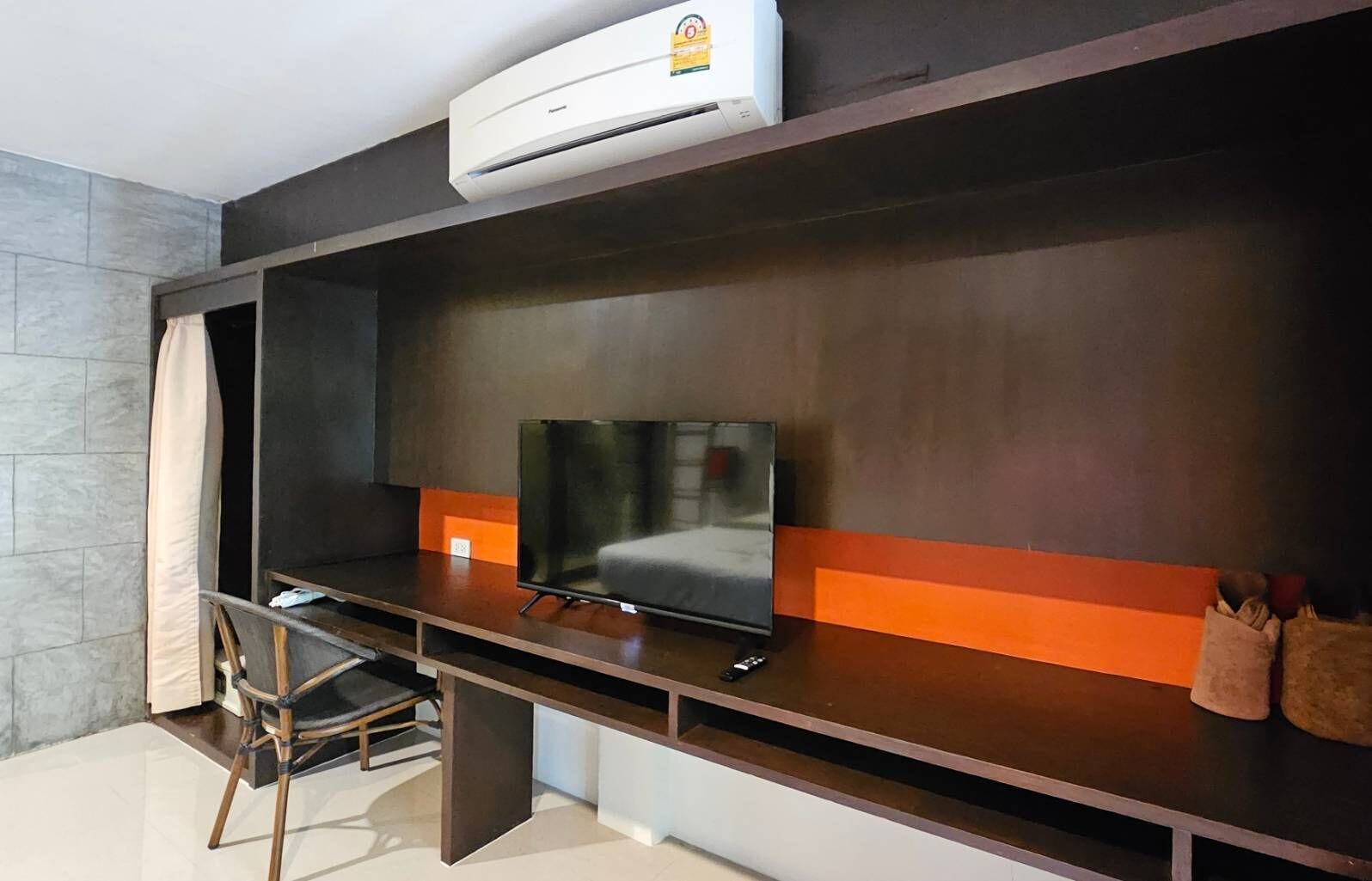 Habitación moderna con televisor de pantalla plana, escritorio, silla y equipo de aire acondicionado instalado en la pared.