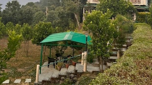 A two-story building with a green roof and a balcony, surrounded by lush greenery and a mountainous backdrop. - Emerald Trail (Nainital)
