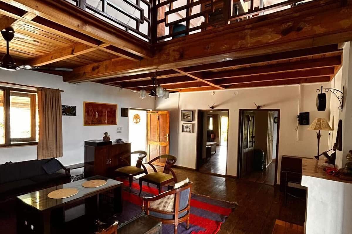 A spacious loft with a high ceiling, exposed wooden beams, a dining area with a table and chairs, and a staircase leading to an upper level.