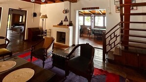 A spacious living area with a high ceiling, wooden beams, a fireplace, and a staircase leading to an upper level. - Emerald Trail (Nainital)