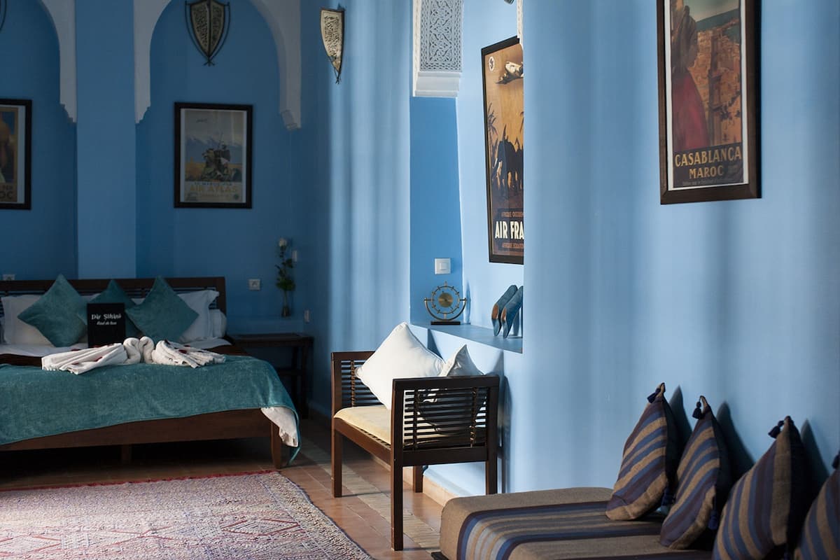 Una habitación con una cama, una silla y un sofá. Hay almohadas y una manta en la cama.