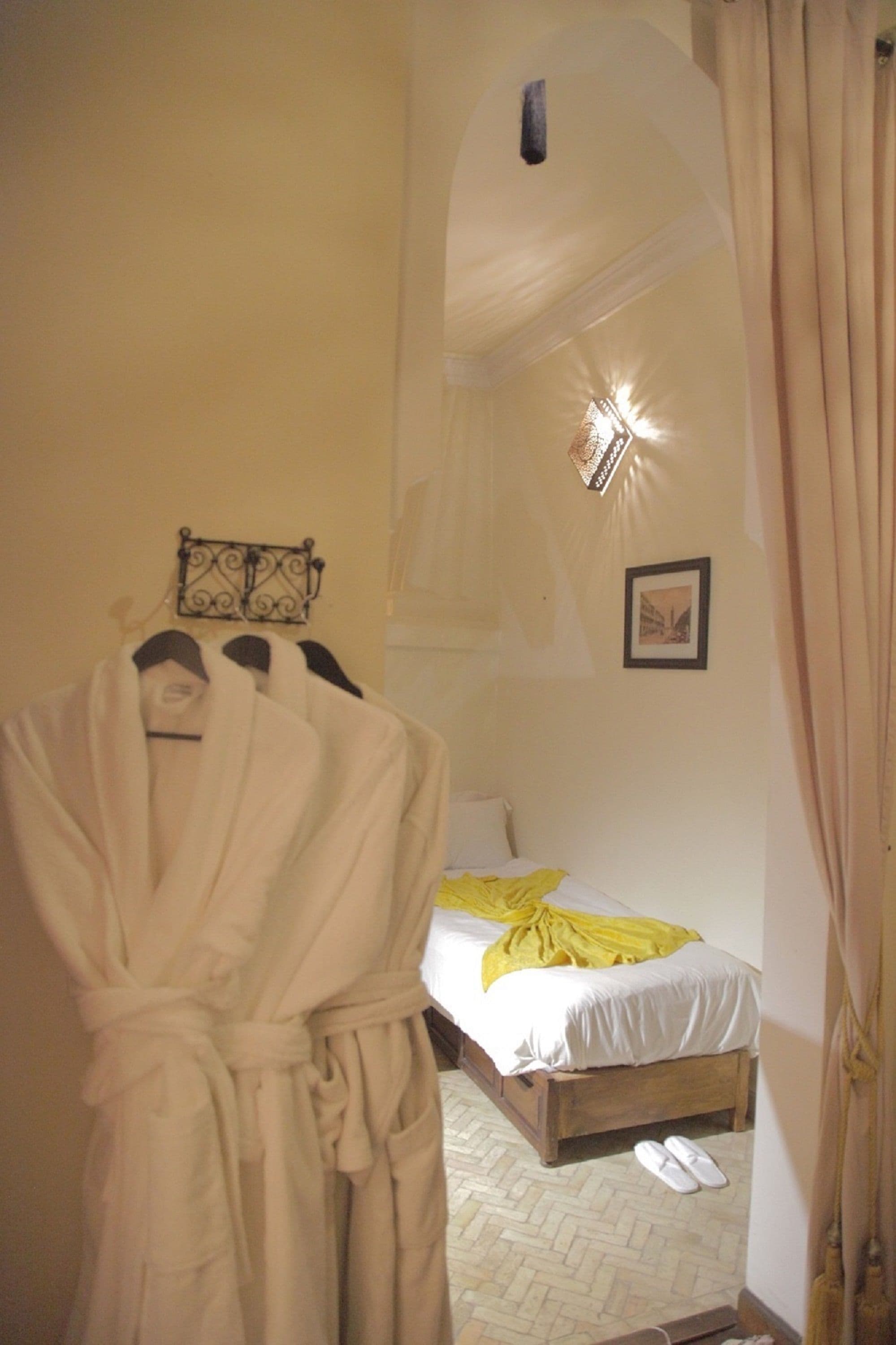 Een hotelkamer met een bed, een badjas hangend aan een rek, en een paar slippers op de vloer.