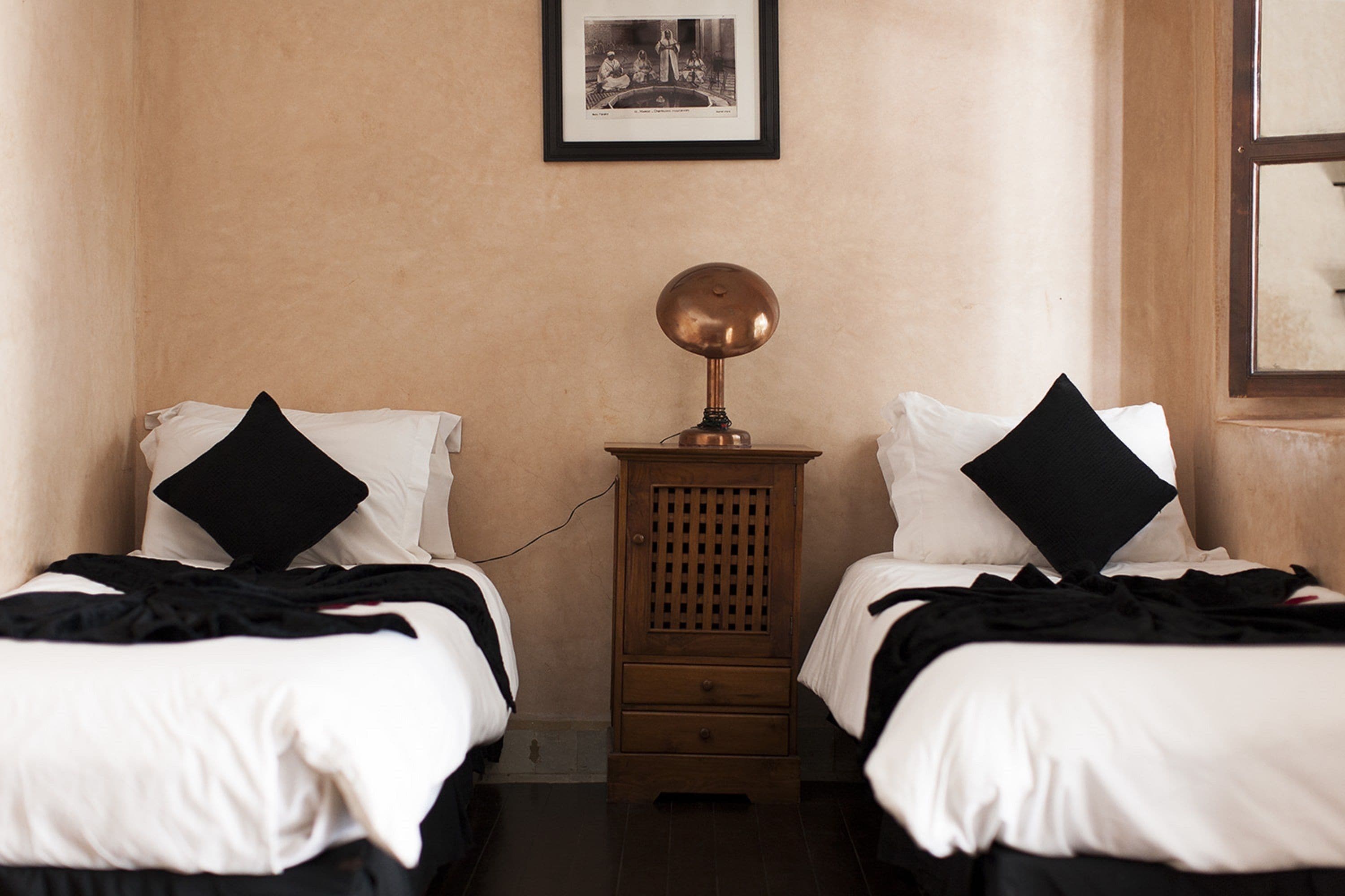 A hotel room with two single beds, a nightstand with a lamp, and a framed picture on the wall.