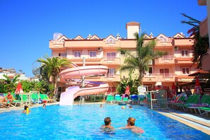 Une piscine avec un toboggan, des chaises longues et un bâtiment doté de balcons en arrière-plan.