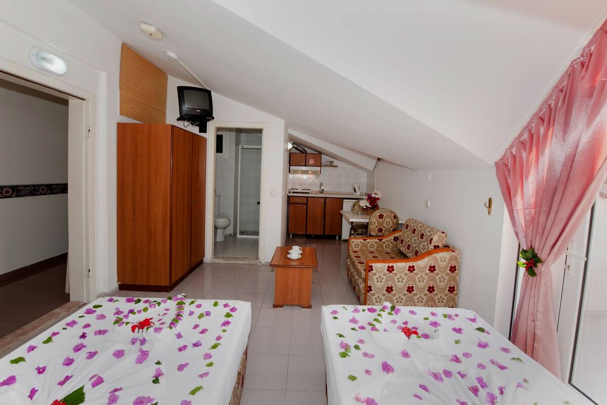Une chambre d’hôtel avec deux lits, une petite table, un canapé, une télévision et, au fond, une kitchenette.