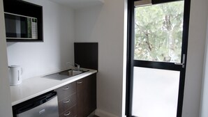 A compact kitchen with a dishwasher, a sink, and a window with a view of trees. - The Sunnyside Tavern, Broadmeadow (Broadmeadow)