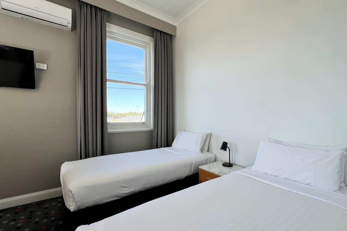 Habitación de hotel con dos camas, un televisor montado en la pared y una ventana con cortinas.