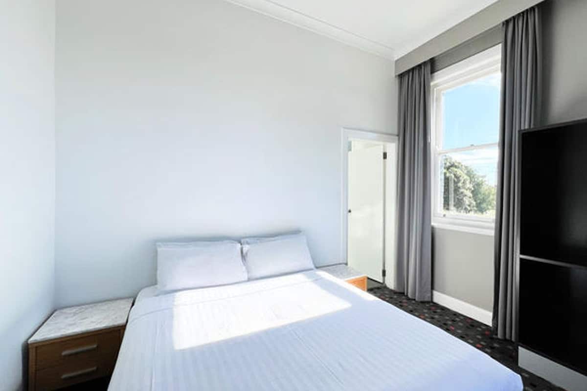 Habitación de hotel con cama, televisor, armario y ventana con cortinas.