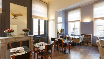 A dining area with tables and chairs, a fireplace, and large windows with blinds.