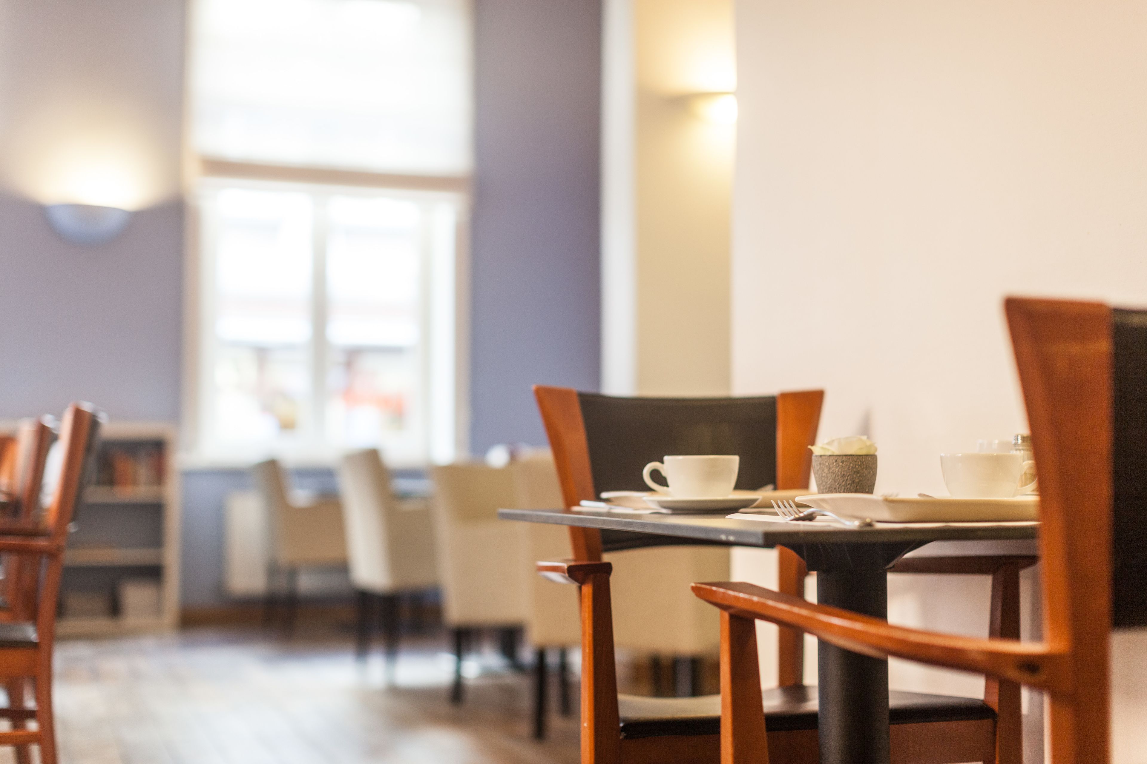 Un coin repas avec des chaises et des tables en bois, une fenêtre avec des stores et un luminaire fixé au mur.