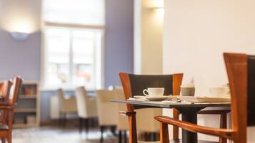 Un coin repas avec des chaises et des tables en bois, une fenêtre avec des stores et un luminaire fixé au mur.