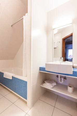 A bathroom with a bathtub, a sink, a mirror, and a shelf with towels. - Hotel Loreto (Bruges)