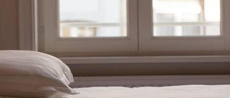 Una cama con ropa de cama blanca en una habitación con un ventanal grande.