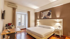 Una habitació d'hotel amb un llit, una taula de nit, una làmpada i un escriptori amb una cadira.