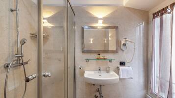 Een moderne badkamer met een douchecabine van glas, een witte wastafel en een spiegel erboven.