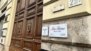 Fachada d'un edifici amb una gran porta de fusta i dos cartells publicitaris que anuncien 'Inn Rome Rooms & Suites'.