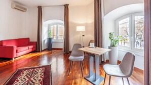 Un saló modern amb un sofà vermell, una taula de menjador amb cadires, una làmpada i finestres grans amb cortines.