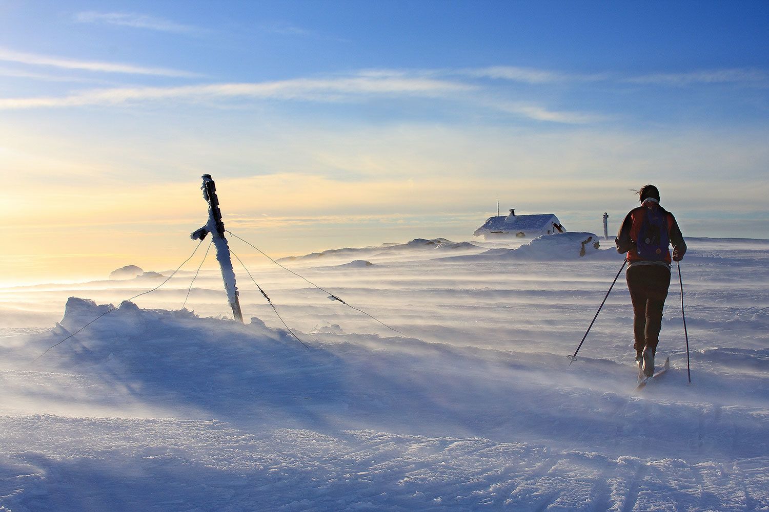 A snowy landscape with a person skiing and another person standing on a snow-covered rock.