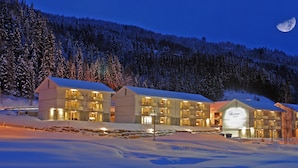 A snow-covered hotel with multiple buildings, a visible sign reading "Hershey Tunet," and a moon in the sky. - Nermo Hotell (Øyer)