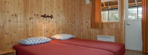 A room with wooden walls, a bed with two pillows, a window with curtains, and a door.