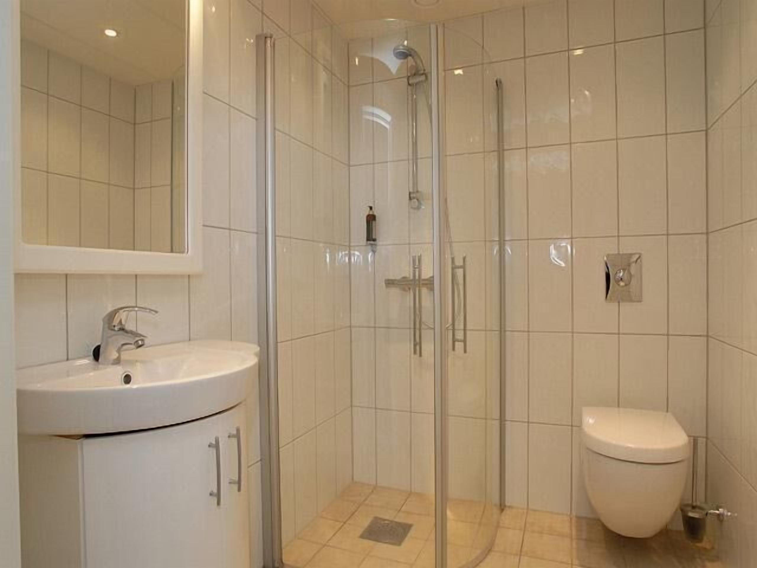 Een moderne badkamer met een douchecabine van glas, een wit wastafelmeubel en een toilet.